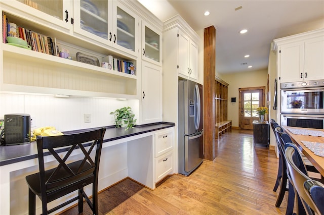 kitchen featuring white cabinetry, built in desk, stainless steel appliances, and light wood-type flooring