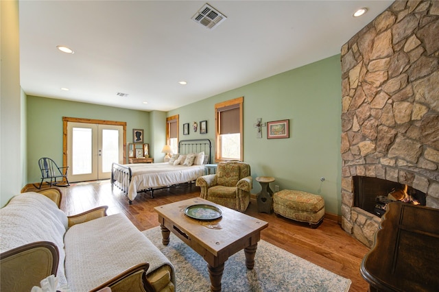 bedroom with a stone fireplace, access to outside, light hardwood / wood-style floors, and french doors