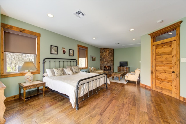 bedroom with a stone fireplace and light hardwood / wood-style floors