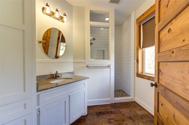 bathroom with wood-type flooring, tiled shower, and vanity