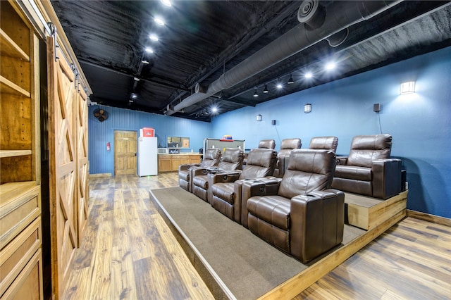 cinema featuring hardwood / wood-style floors, rail lighting, and a barn door