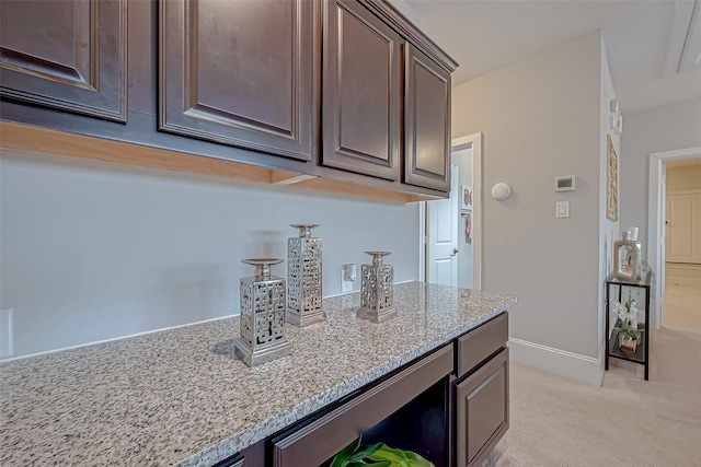 kitchen featuring light stone countertops, dark brown cabinetry, light carpet, and baseboards