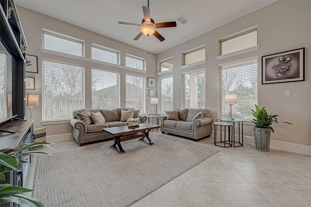 living room with ceiling fan, light tile patterned flooring, a towering ceiling, visible vents, and baseboards