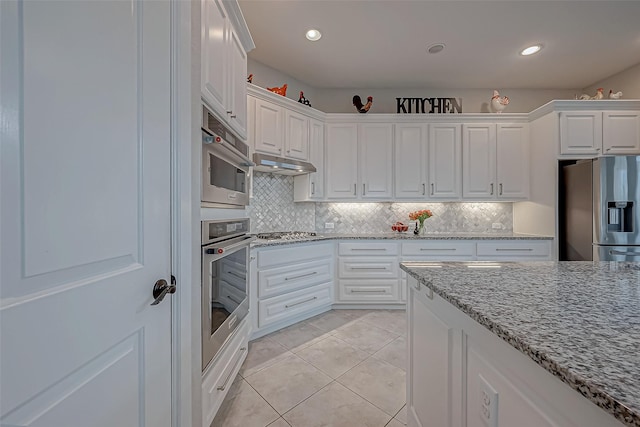 kitchen featuring stainless steel appliances, light tile patterned flooring, white cabinetry, light stone countertops, and under cabinet range hood