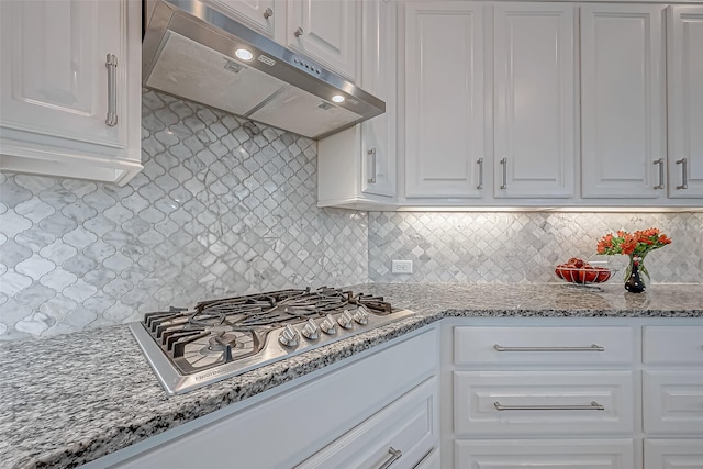 kitchen featuring tasteful backsplash, light stone countertops, under cabinet range hood, stainless steel gas stovetop, and white cabinetry