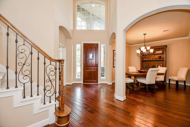 entryway featuring crown molding, a towering ceiling, dark hardwood / wood-style flooring, and a chandelier