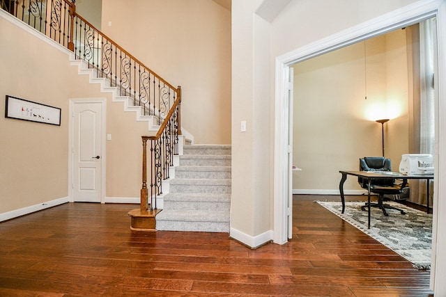 stairs featuring hardwood / wood-style floors, baseboards, and a towering ceiling