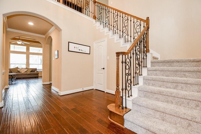 stairs with ceiling fan, ornamental molding, wood-type flooring, and a towering ceiling