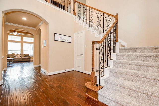 stairway featuring baseboards, ornamental molding, a high ceiling, arched walkways, and wood-type flooring