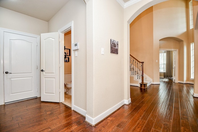 hall featuring baseboards, arched walkways, dark wood-type flooring, and stairway