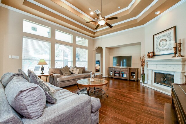 living room featuring a high ceiling, ornamental molding, ceiling fan, a tray ceiling, and dark wood-type flooring