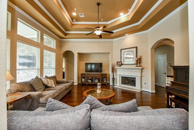 living room with dark wood-type flooring, ceiling fan, ornamental molding, and a tray ceiling