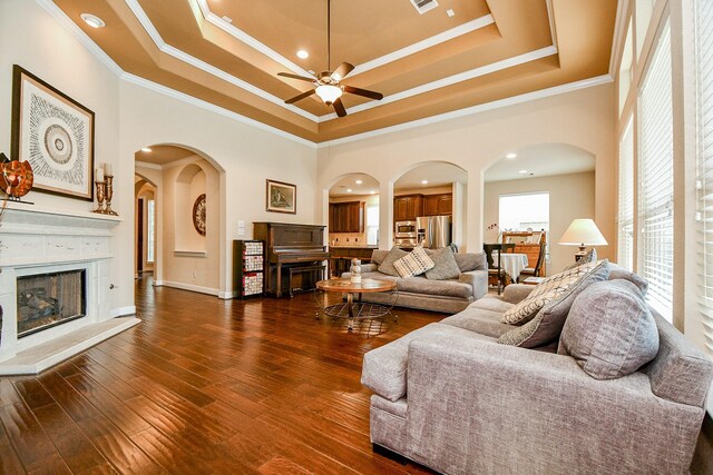 living room featuring a towering ceiling, ornamental molding, dark wood-type flooring, and a tray ceiling