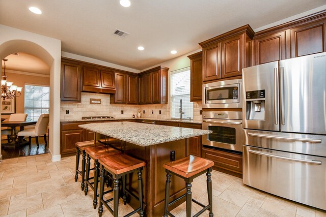 kitchen with sink, stainless steel appliances, tasteful backsplash, light stone countertops, and a kitchen island