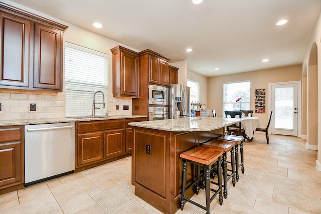 kitchen with a breakfast bar, a sink, a kitchen island, stainless steel appliances, and decorative backsplash