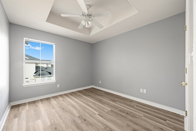 unfurnished room featuring a tray ceiling, light hardwood / wood-style floors, and ceiling fan