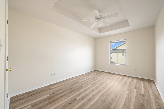 empty room featuring a raised ceiling, ceiling fan, and light hardwood / wood-style flooring