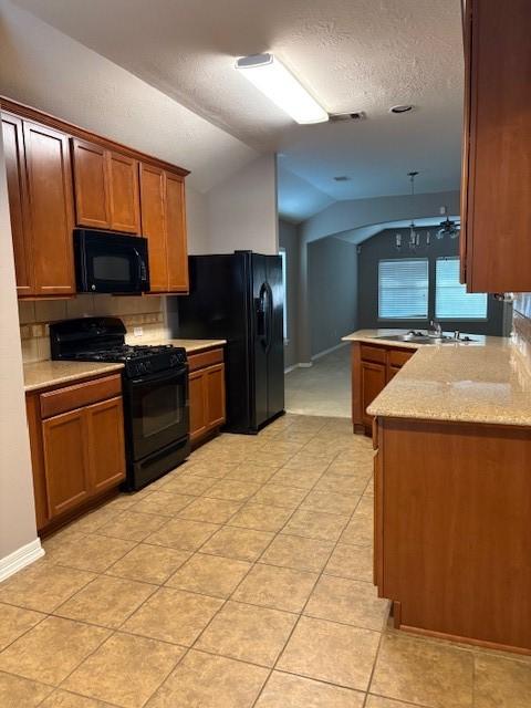 kitchen featuring lofted ceiling, sink, light stone counters, kitchen peninsula, and black appliances