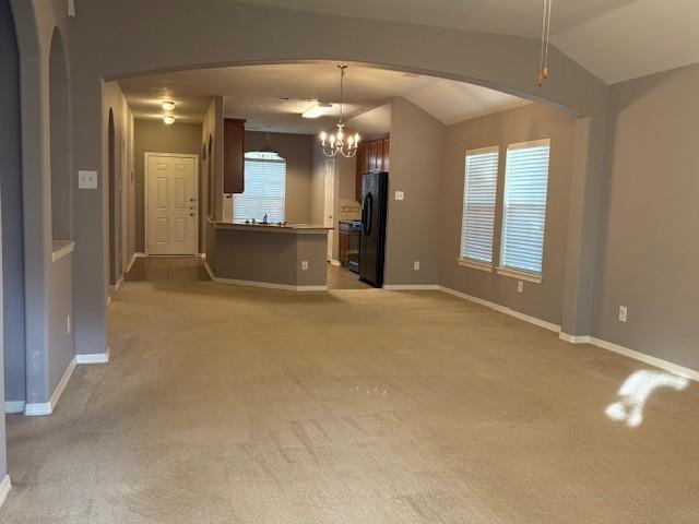 unfurnished living room with light colored carpet, a chandelier, and vaulted ceiling