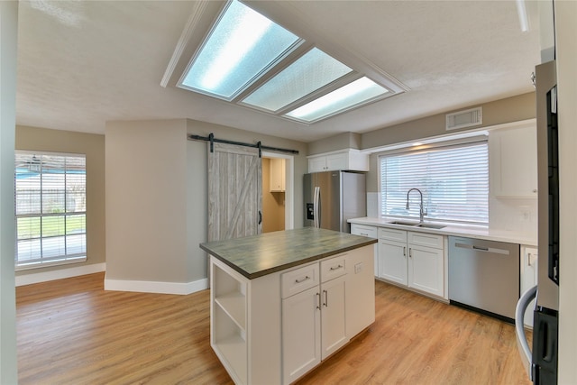 kitchen featuring appliances with stainless steel finishes, white cabinetry, sink, a center island, and a barn door