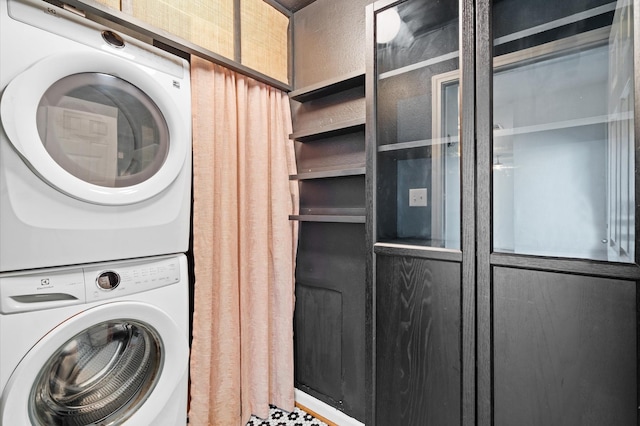 clothes washing area with laundry area, stacked washer and clothes dryer, and a textured wall