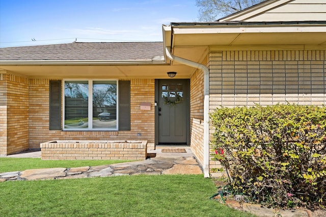 entrance to property with brick siding, a lawn, and a shingled roof