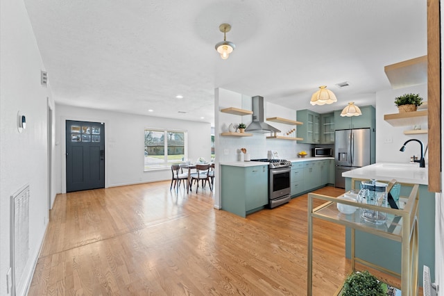 kitchen featuring light wood finished floors, green cabinetry, open shelves, appliances with stainless steel finishes, and wall chimney range hood