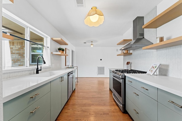 kitchen featuring visible vents, open shelves, a sink, stainless steel appliances, and wall chimney exhaust hood