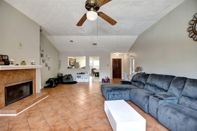 living room with a tiled fireplace, vaulted ceiling, tile patterned floors, and a textured ceiling