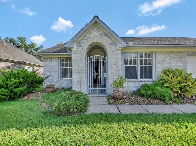 doorway to property featuring a garage, a yard, roof with shingles, and brick siding