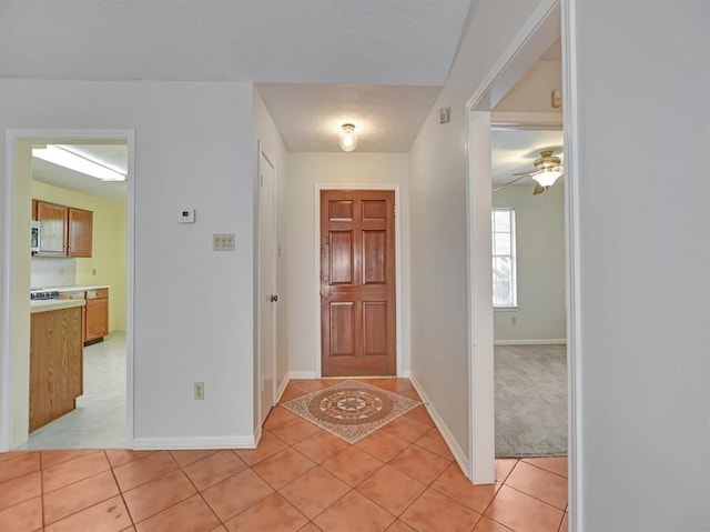 entrance foyer with light tile patterned floors, ceiling fan, baseboards, and light colored carpet