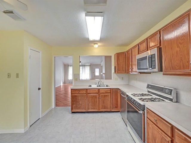 kitchen with light countertops, appliances with stainless steel finishes, a sink, and brown cabinets