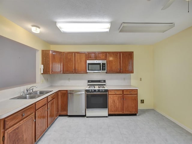 kitchen featuring ceiling fan, stainless steel appliances, a sink, light countertops, and brown cabinetry