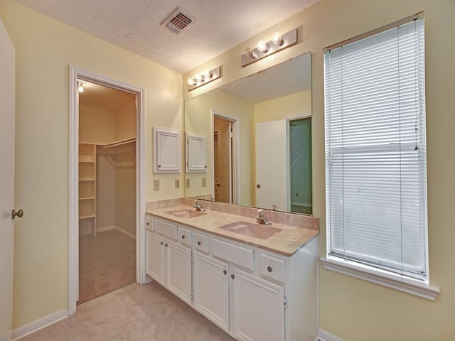 full bath with a textured ceiling, visible vents, a walk in closet, and a sink