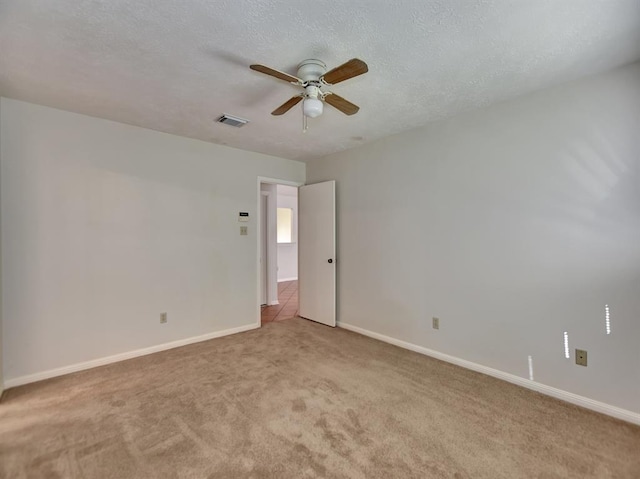 spare room with a textured ceiling, light carpet, a ceiling fan, visible vents, and baseboards