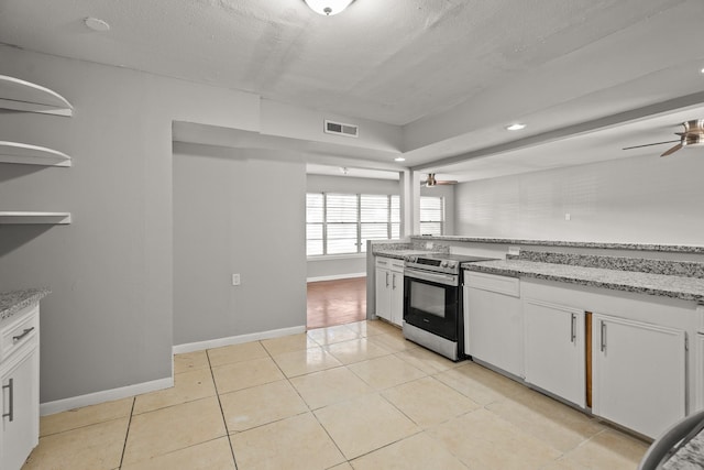 kitchen with light stone counters, light tile patterned floors, stainless steel electric range, and white cabinets