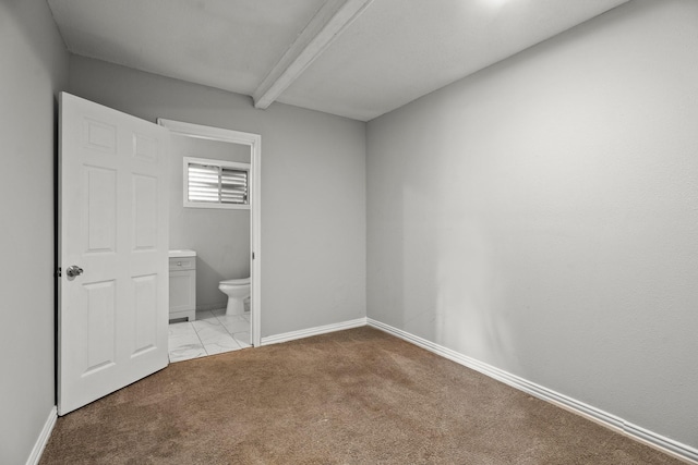 unfurnished bedroom with beamed ceiling, ensuite bathroom, and light carpet