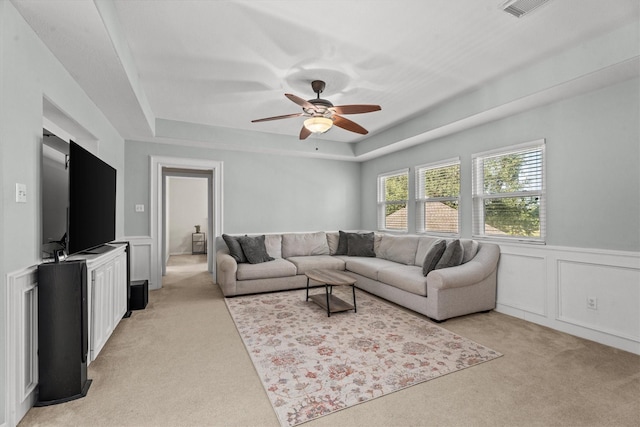 living room featuring light carpet, ceiling fan, and a tray ceiling