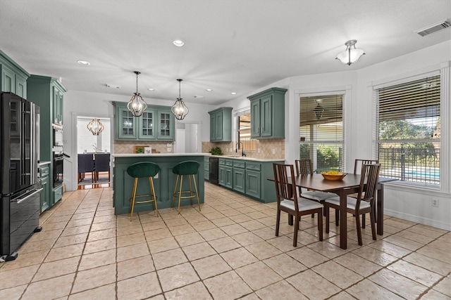 kitchen with a breakfast bar area, green cabinets, backsplash, hanging light fixtures, and black appliances