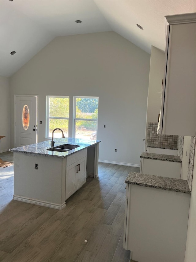 kitchen with sink, light stone countertops, white cabinets, a center island with sink, and dark hardwood / wood-style flooring