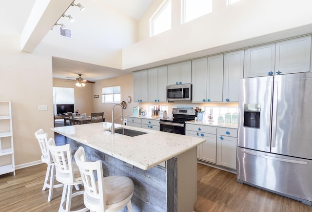 kitchen featuring sink, gray cabinetry, light stone counters, a center island with sink, and appliances with stainless steel finishes