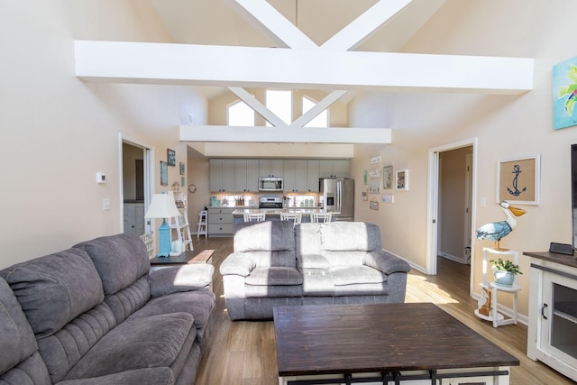 living room featuring high vaulted ceiling, light hardwood / wood-style floors, and beamed ceiling