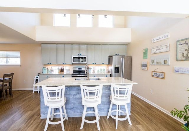 kitchen featuring sink, gray cabinetry, light stone counters, stainless steel appliances, and a kitchen island with sink