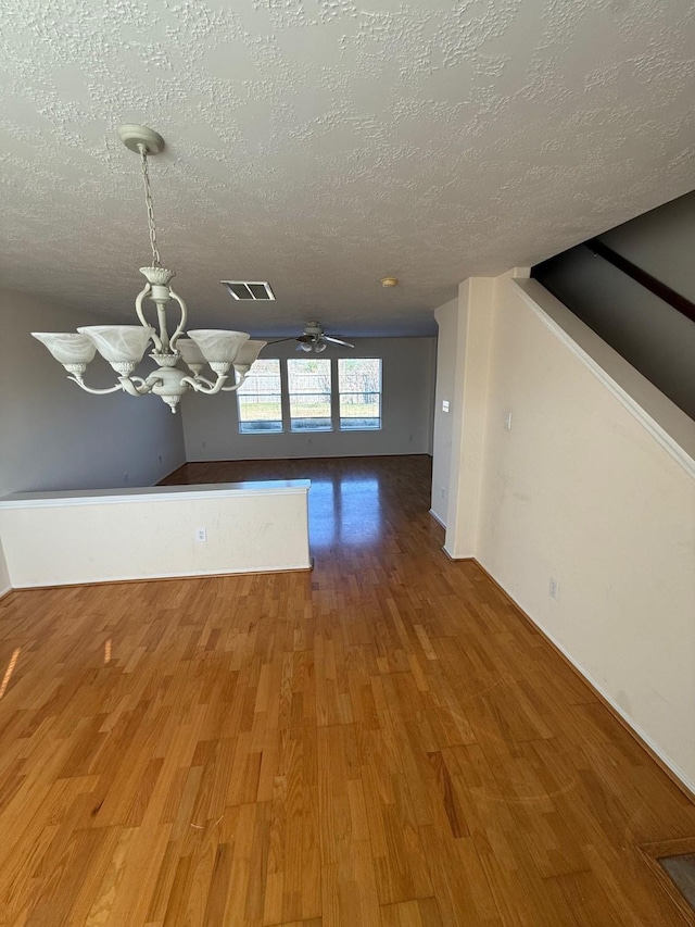 unfurnished dining area with wood-type flooring, ceiling fan with notable chandelier, and a textured ceiling