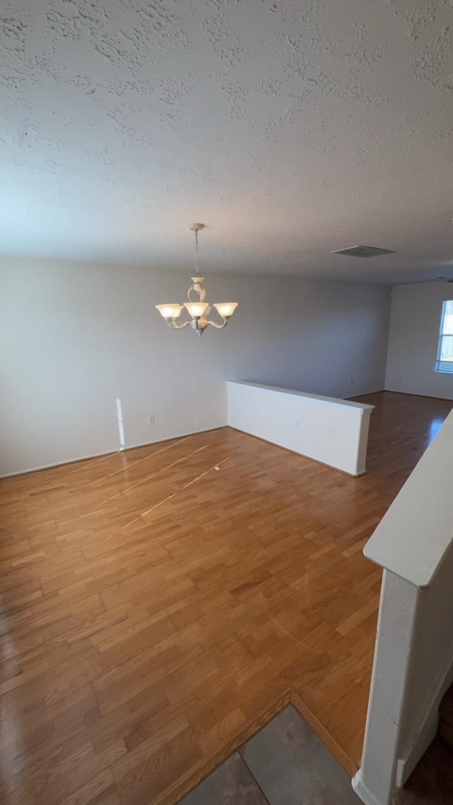 unfurnished room featuring hardwood / wood-style floors, a textured ceiling, and a chandelier