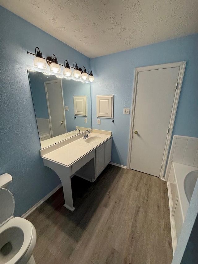 bathroom featuring toilet, a textured ceiling, vanity, a tub, and hardwood / wood-style floors