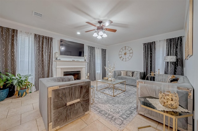 tiled living room featuring crown molding, ceiling fan, and a tiled fireplace