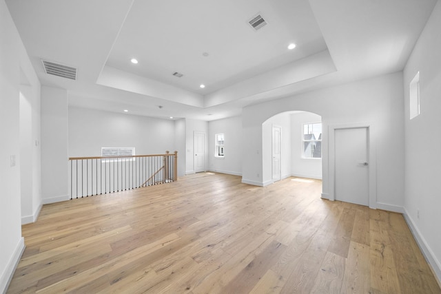 spare room featuring a tray ceiling, arched walkways, visible vents, and light wood finished floors