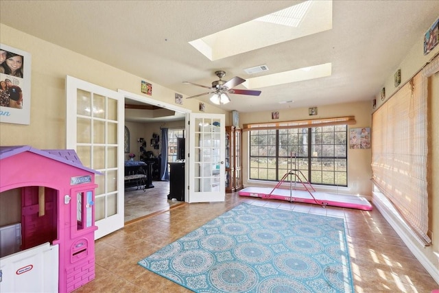 playroom with ceiling fan, tile patterned flooring, a skylight, a textured ceiling, and french doors