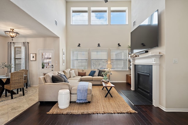 living room with dark wood-type flooring, a towering ceiling, and a tile fireplace